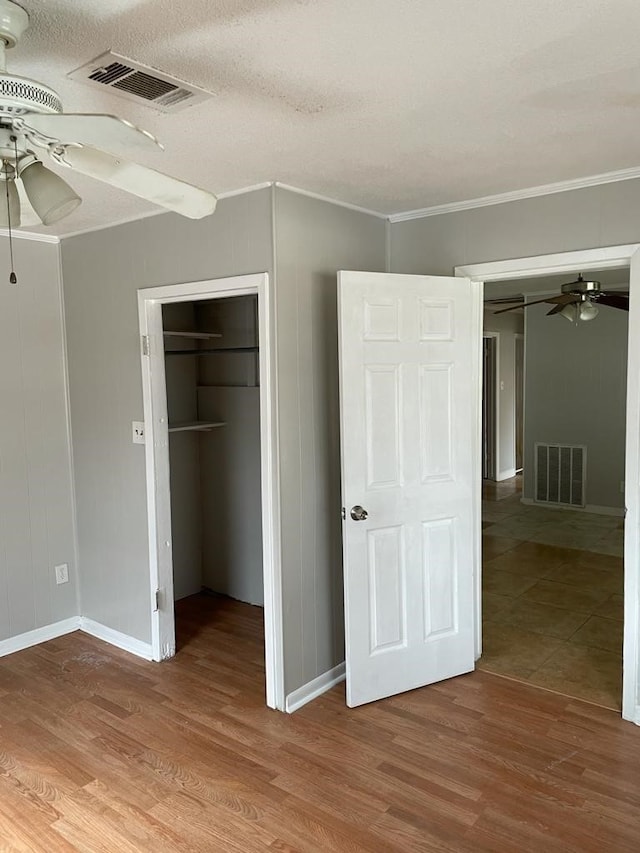 unfurnished bedroom with a closet, ceiling fan, hardwood / wood-style flooring, and crown molding