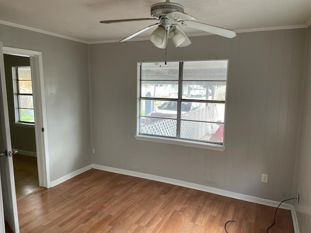 empty room featuring ornamental molding, wooden walls, ceiling fan, and hardwood / wood-style flooring