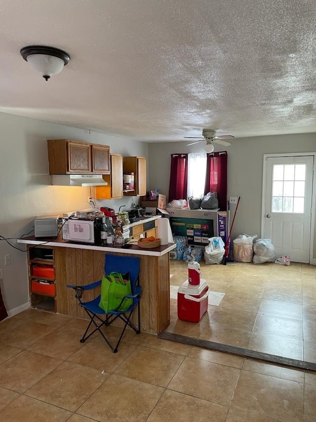 kitchen with light tile patterned floors, kitchen peninsula, ceiling fan, and a textured ceiling