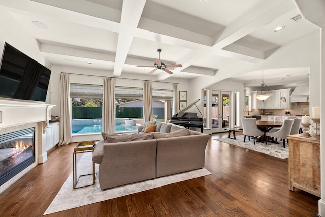 living room featuring ceiling fan, beam ceiling, dark wood-type flooring, and coffered ceiling