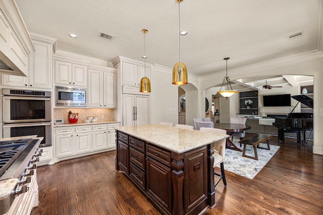 kitchen with hanging light fixtures, a breakfast bar area, built in appliances, and dark hardwood / wood-style flooring