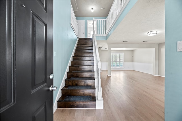 stairs with a textured ceiling, decorative columns, and hardwood / wood-style flooring