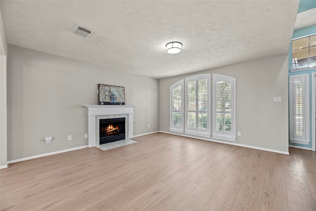 unfurnished living room featuring light hardwood / wood-style floors, a tile fireplace, and a textured ceiling