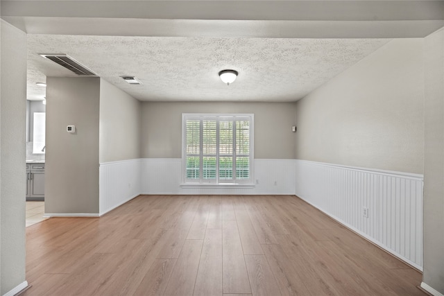 spare room featuring light wood-type flooring and a textured ceiling