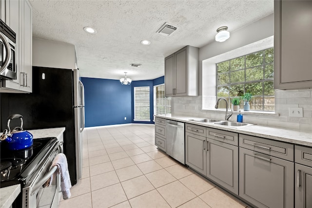 kitchen with appliances with stainless steel finishes, gray cabinetry, decorative backsplash, a textured ceiling, and sink