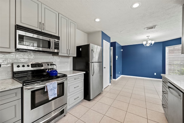 kitchen featuring appliances with stainless steel finishes, a chandelier, gray cabinets, and tasteful backsplash