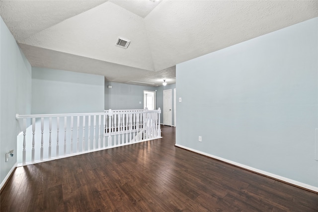 unfurnished room with a textured ceiling, wood-type flooring, and lofted ceiling