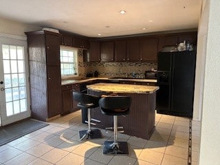 kitchen with black fridge, light tile patterned floors, a kitchen breakfast bar, a kitchen island, and dark brown cabinets