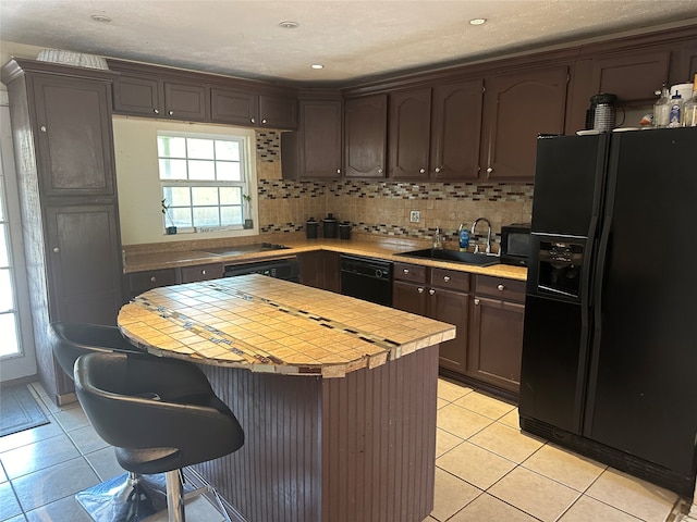 kitchen with dark brown cabinetry, black appliances, sink, light tile patterned floors, and backsplash