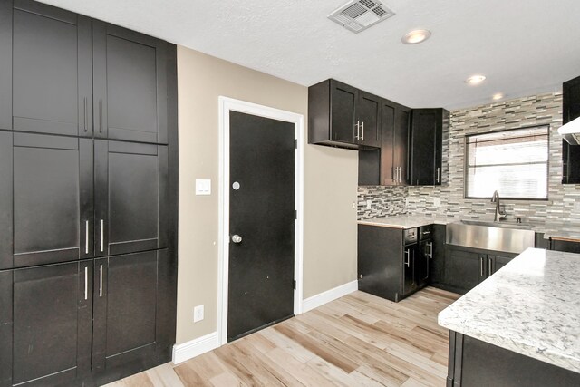 kitchen with decorative backsplash, a textured ceiling, light hardwood / wood-style floors, and sink