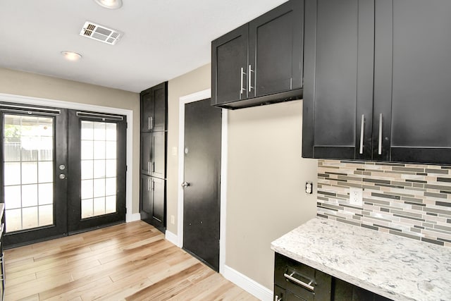 kitchen with light stone countertops, light hardwood / wood-style flooring, french doors, and tasteful backsplash