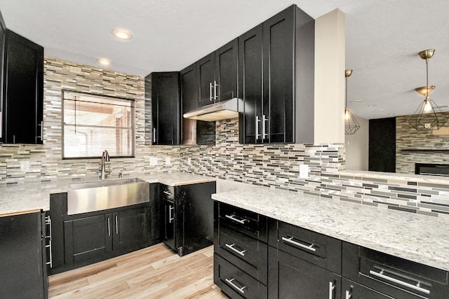 kitchen with decorative backsplash, light stone counters, light hardwood / wood-style floors, and sink