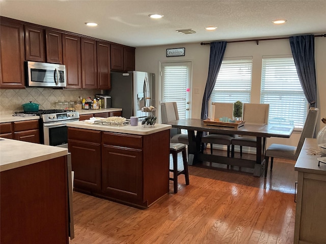 kitchen featuring a kitchen island, light hardwood / wood-style floors, tasteful backsplash, a healthy amount of sunlight, and stainless steel appliances