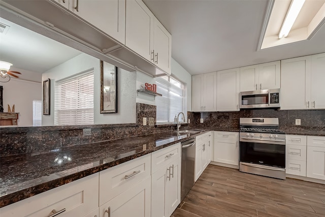 kitchen with sink, white cabinetry, stainless steel appliances, dark wood-type flooring, and dark stone countertops