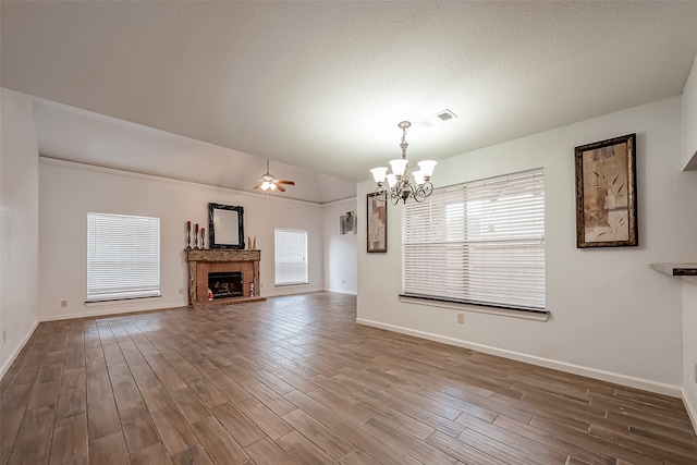 unfurnished living room featuring dark wood-type flooring, a brick fireplace, ceiling fan with notable chandelier, and a healthy amount of sunlight