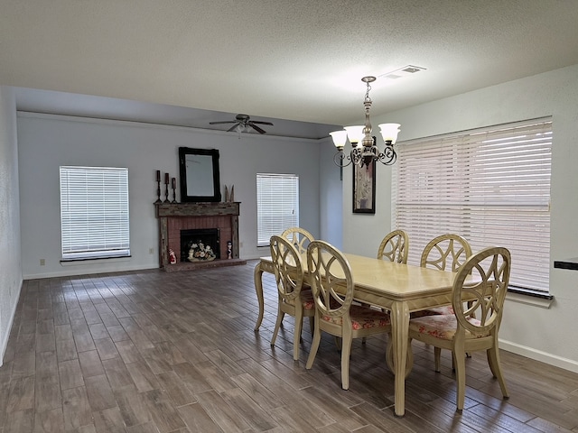 dining area with a textured ceiling, ceiling fan with notable chandelier, a fireplace, and wood-type flooring