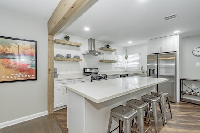 kitchen featuring white cabinets, a kitchen island, wall chimney exhaust hood, appliances with stainless steel finishes, and a breakfast bar area