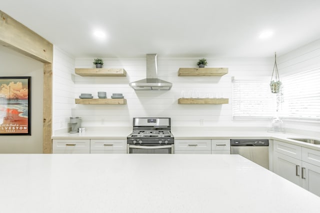 kitchen featuring wall chimney exhaust hood, stainless steel appliances, white cabinets, and tasteful backsplash