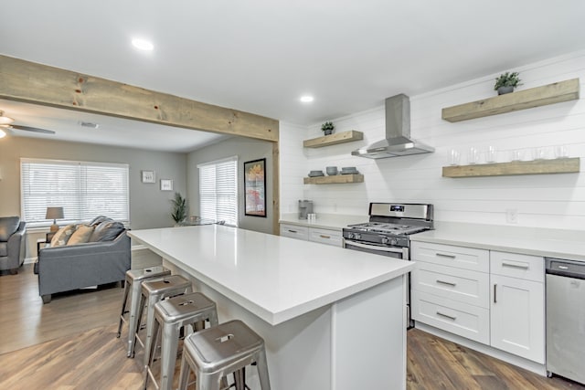 kitchen with dark wood-type flooring, white cabinetry, wall chimney range hood, a kitchen breakfast bar, and stainless steel appliances