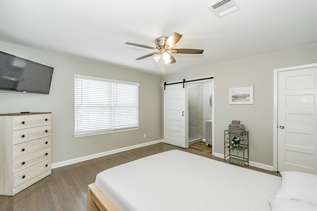 bedroom featuring a barn door, connected bathroom, dark hardwood / wood-style flooring, and ceiling fan