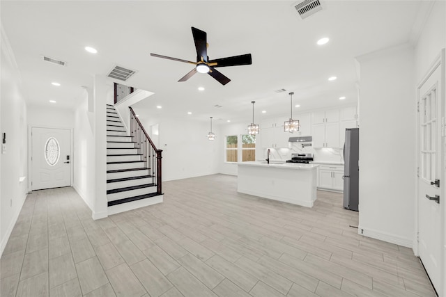 unfurnished living room with ceiling fan with notable chandelier, light hardwood / wood-style flooring, and crown molding