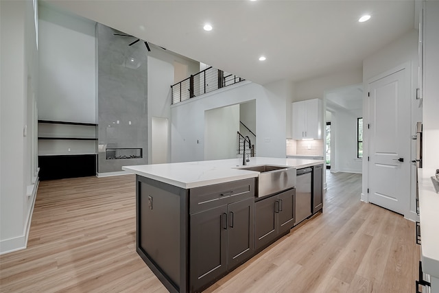 kitchen featuring an island with sink, sink, stainless steel dishwasher, white cabinetry, and light hardwood / wood-style floors