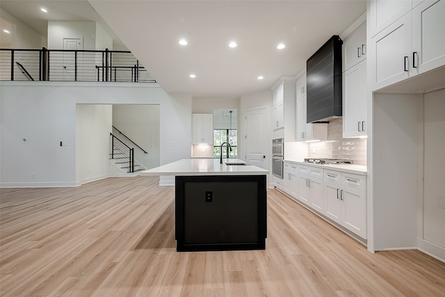 kitchen with a kitchen island with sink, white cabinetry, and light hardwood / wood-style flooring