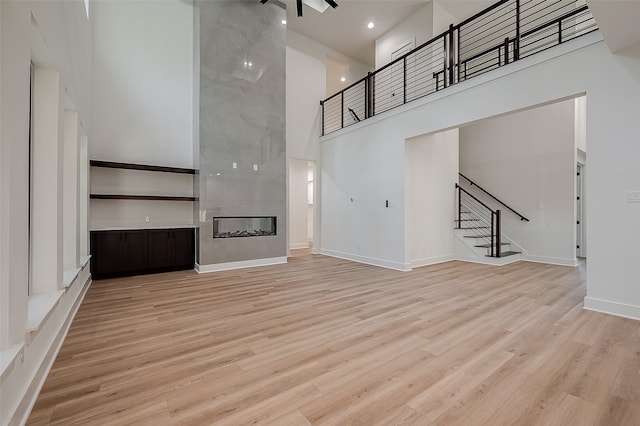 unfurnished living room featuring ceiling fan, a multi sided fireplace, a towering ceiling, and light hardwood / wood-style floors