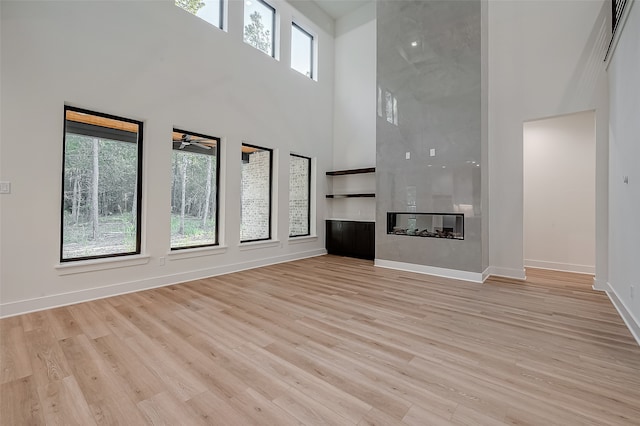 unfurnished living room featuring light hardwood / wood-style floors, plenty of natural light, a high ceiling, and a fireplace