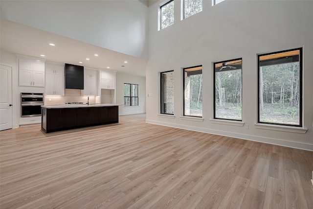 unfurnished living room featuring light wood-type flooring, a towering ceiling, ceiling fan, and sink