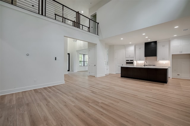 unfurnished living room with light wood-type flooring, a towering ceiling, and sink