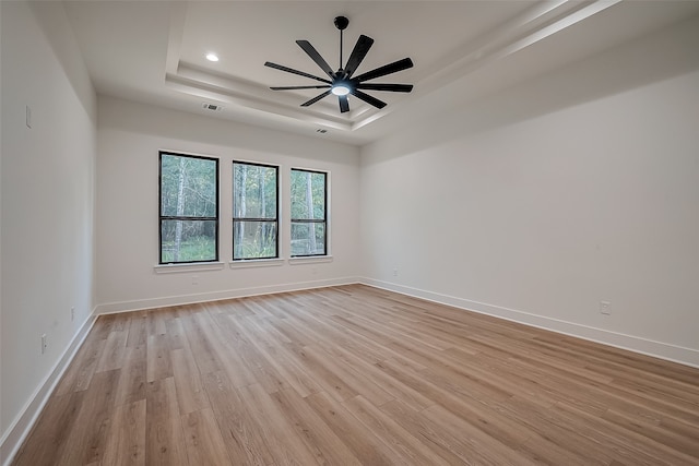 spare room featuring a raised ceiling, light hardwood / wood-style floors, and ceiling fan