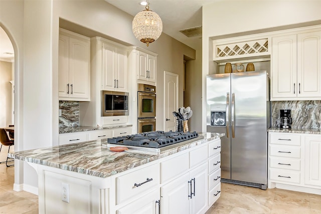 kitchen with decorative backsplash, hanging light fixtures, light stone countertops, a center island, and appliances with stainless steel finishes