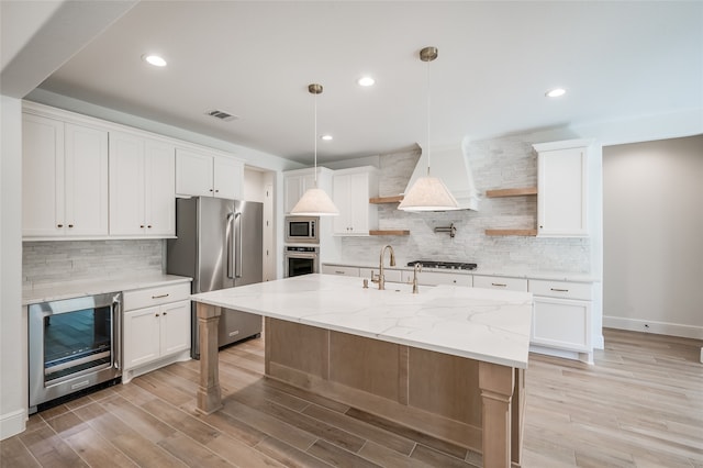 kitchen with white cabinetry, stainless steel appliances, wine cooler, light hardwood / wood-style flooring, and a center island with sink