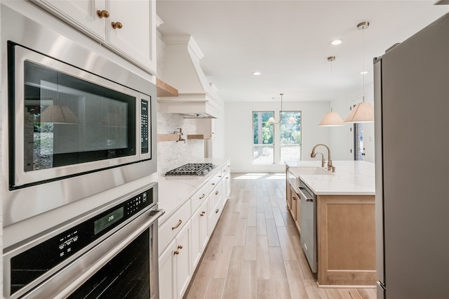 kitchen featuring light stone countertops, white cabinetry, stainless steel appliances, and decorative light fixtures