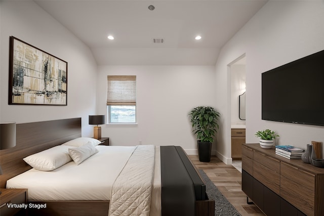 bedroom featuring ensuite bathroom, lofted ceiling, and light hardwood / wood-style flooring