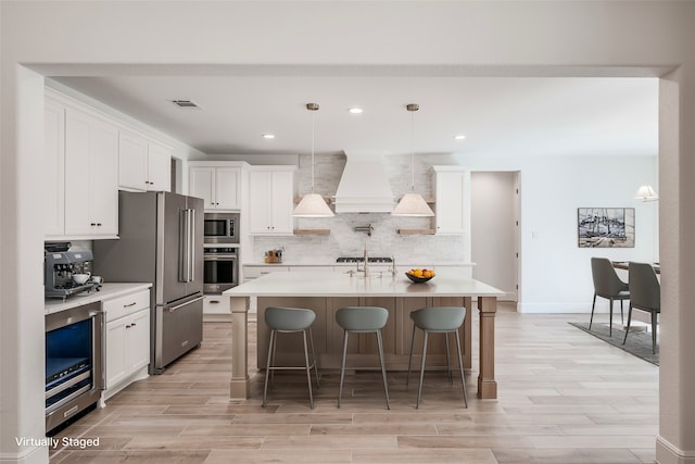 kitchen with decorative light fixtures, white cabinetry, stainless steel appliances, and a kitchen island with sink