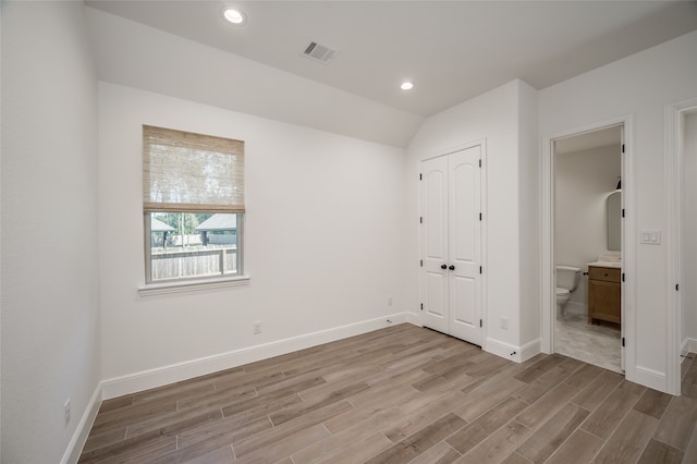 unfurnished bedroom featuring ensuite bathroom, light hardwood / wood-style floors, lofted ceiling, and a closet