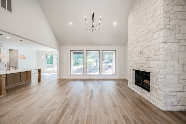 unfurnished living room featuring a stone fireplace, sink, high vaulted ceiling, and light wood-type flooring