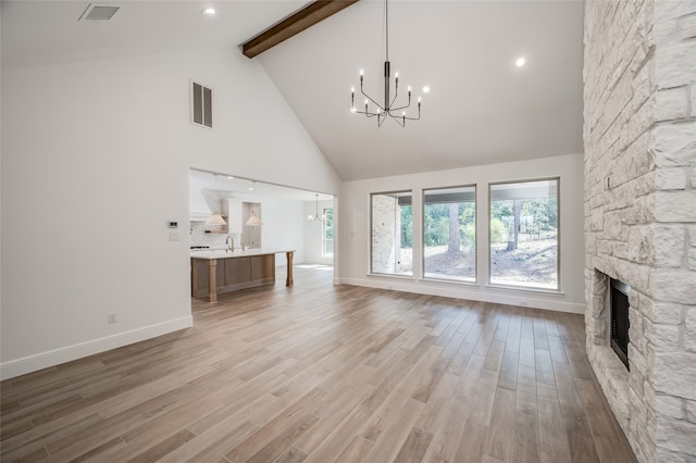 unfurnished living room with beam ceiling, high vaulted ceiling, light hardwood / wood-style flooring, and a stone fireplace