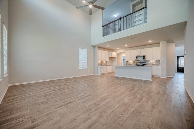 3423 Hackberry Tree Ln, Katy, TX 77449 - unfurnished living room with a high ceiling, light wood-style floors, a ceiling fan, and baseboards
