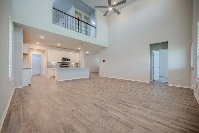 3423 Hackberry Tree Ln, Katy, TX 77449 - unfurnished living room with a towering ceiling, a ceiling fan, light wood-style floors, and baseboards