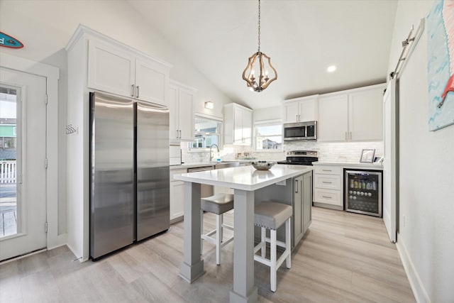 kitchen featuring lofted ceiling, beverage cooler, stainless steel appliances, white cabinets, and a kitchen bar