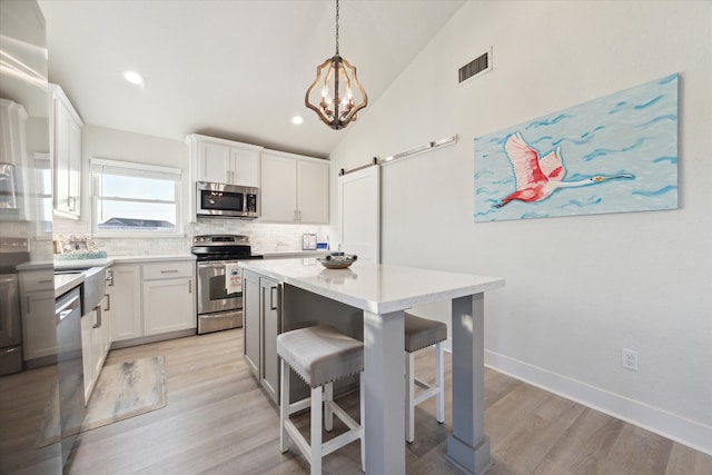 kitchen with a center island, stainless steel appliances, white cabinetry, a barn door, and vaulted ceiling