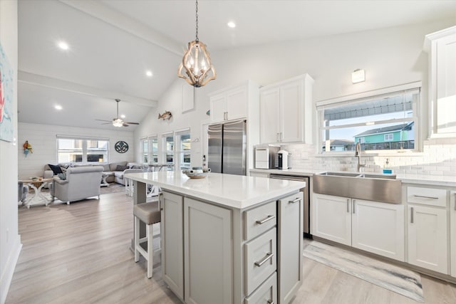 kitchen with white cabinets, hanging light fixtures, sink, stainless steel refrigerator, and a center island