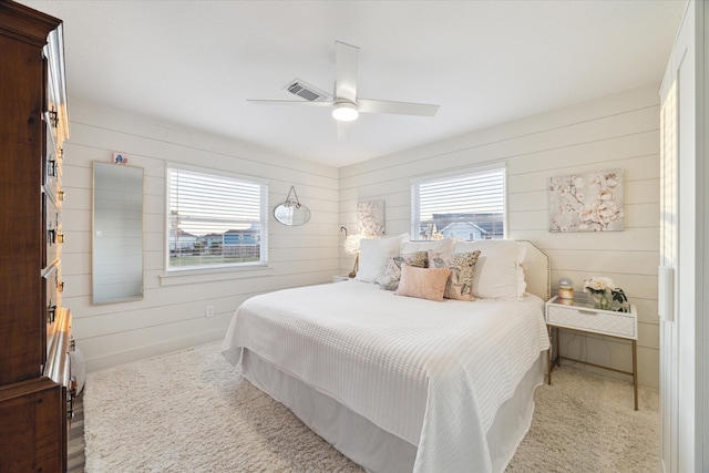 carpeted bedroom featuring multiple windows, ceiling fan, and wood walls