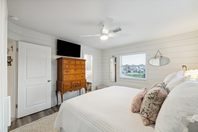 bedroom featuring dark wood-type flooring, connected bathroom, wooden walls, and ceiling fan