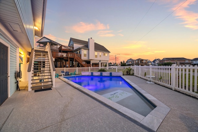 pool at dusk with a wooden deck and a patio