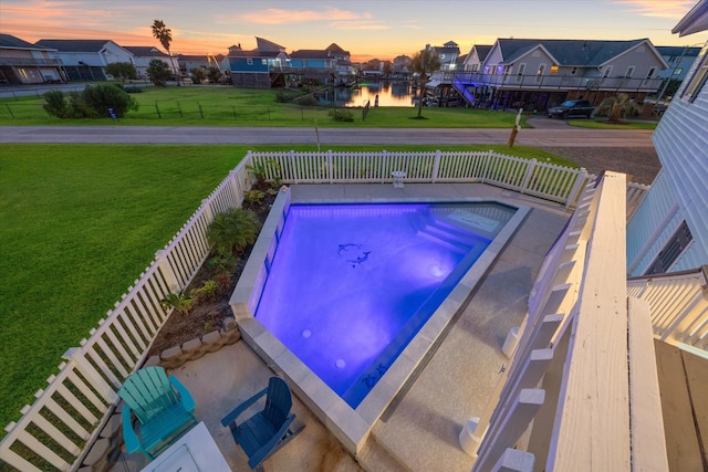 pool at dusk featuring a water view, a jacuzzi, and a yard