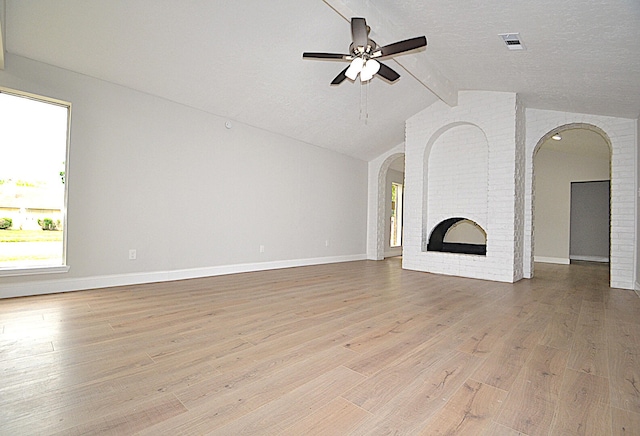 unfurnished living room featuring light wood-type flooring, a textured ceiling, a fireplace, vaulted ceiling with beams, and ceiling fan